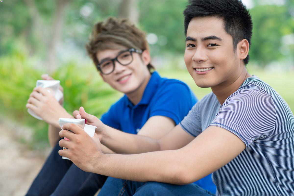 Male Asian friends eating lunch on the curb