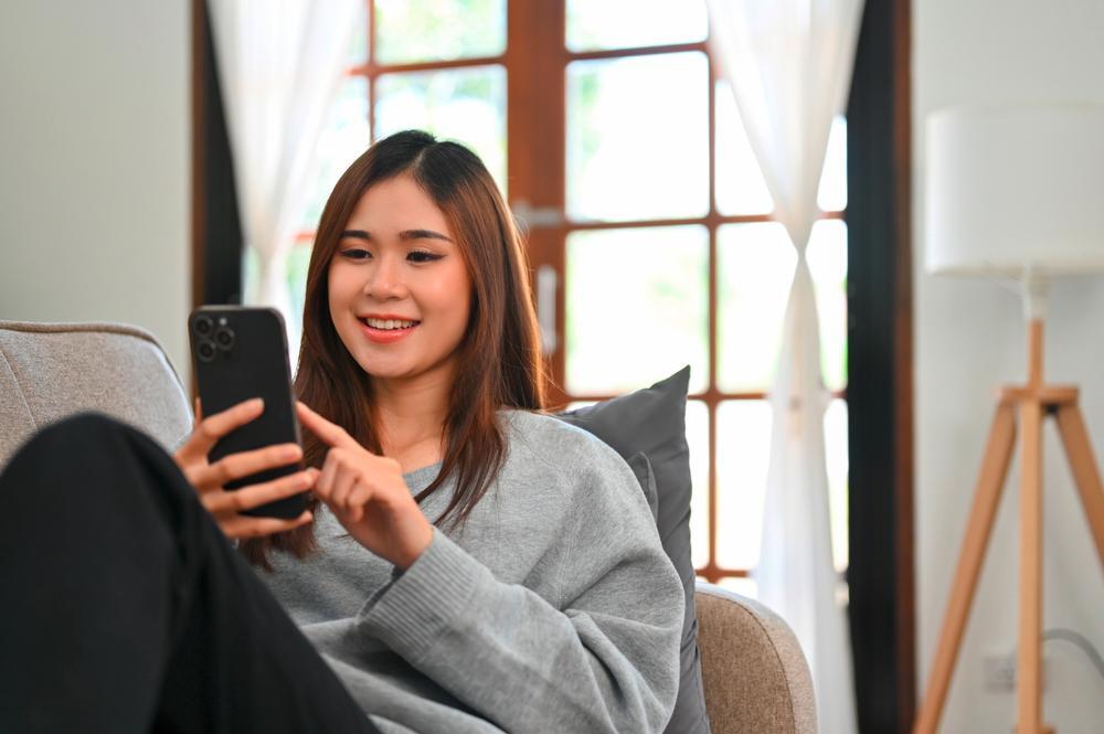 Smiling woman playing with her phone while sitting on a sofa.