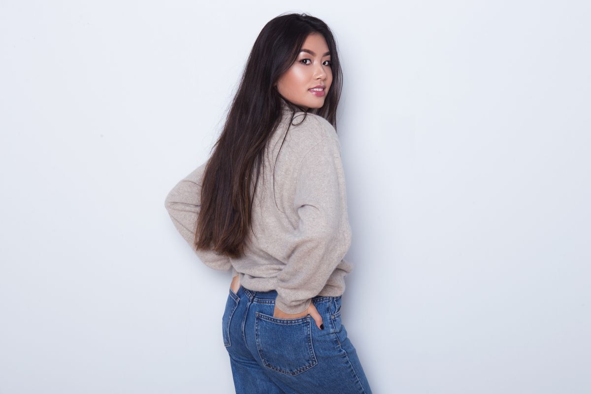 Asian woman with long hair posing from the back against a gray background.