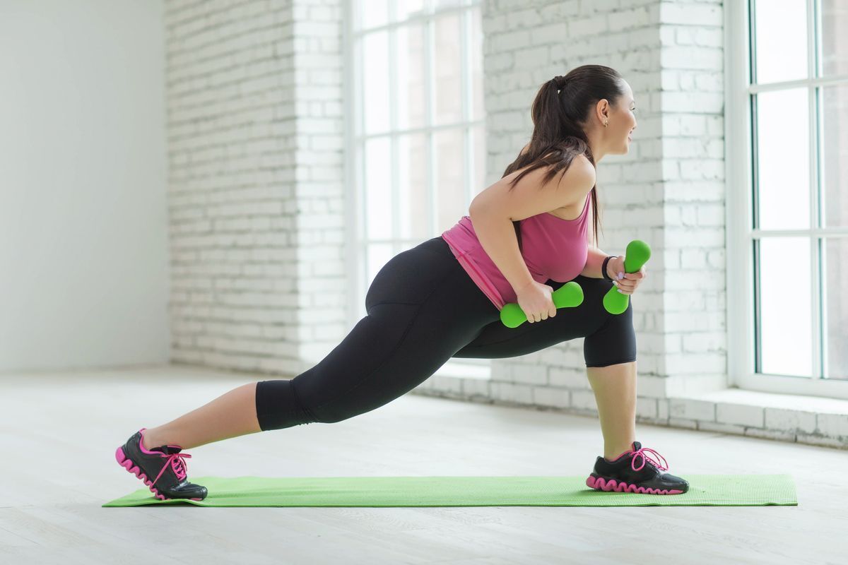 Woman happily exercising with barbels in a bright room while smiling and looking out the window.