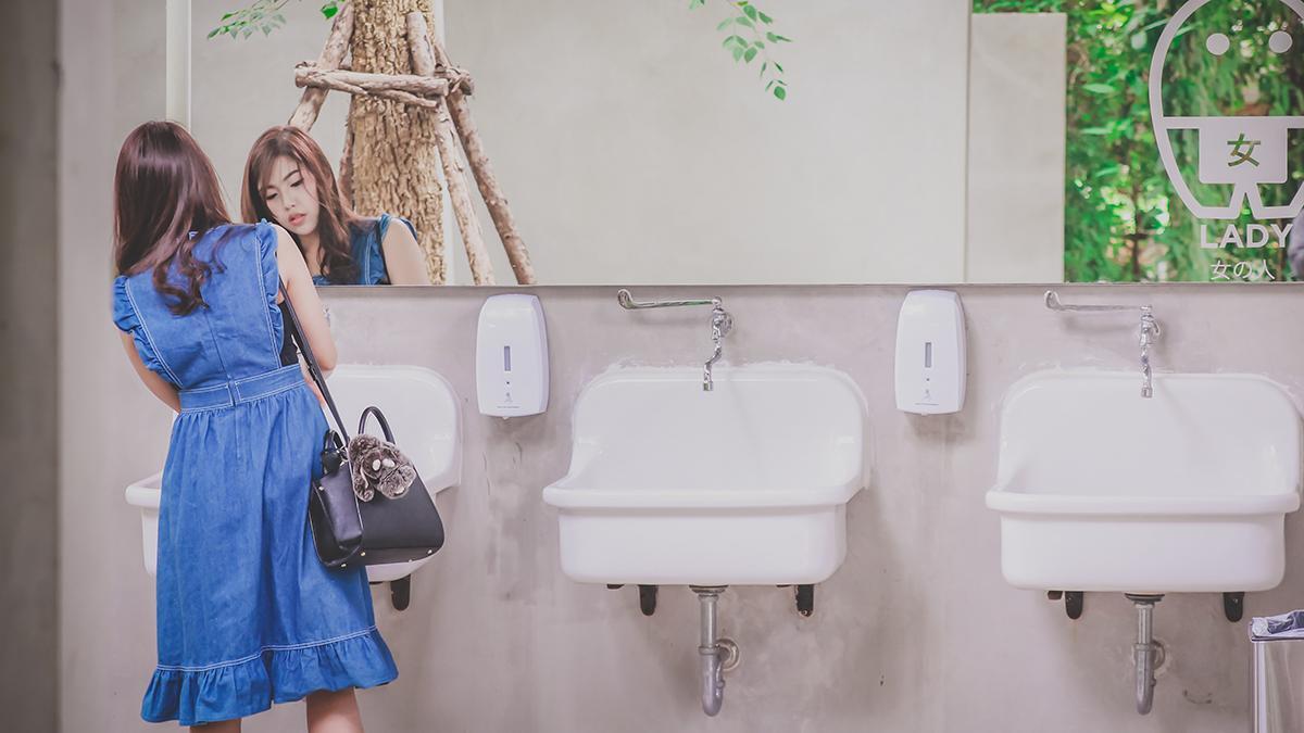 Asian woman in blue dress washing hands in public restroom