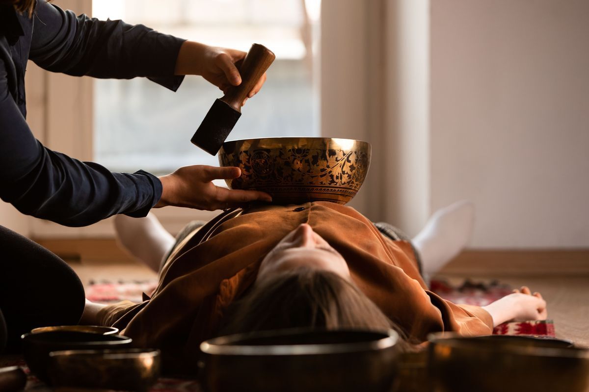 Woman getting sound bath therapy with Tibetan singing bowl.