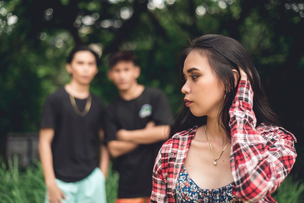Two men staring at a nervous, uncomfortable girl from a distance. 