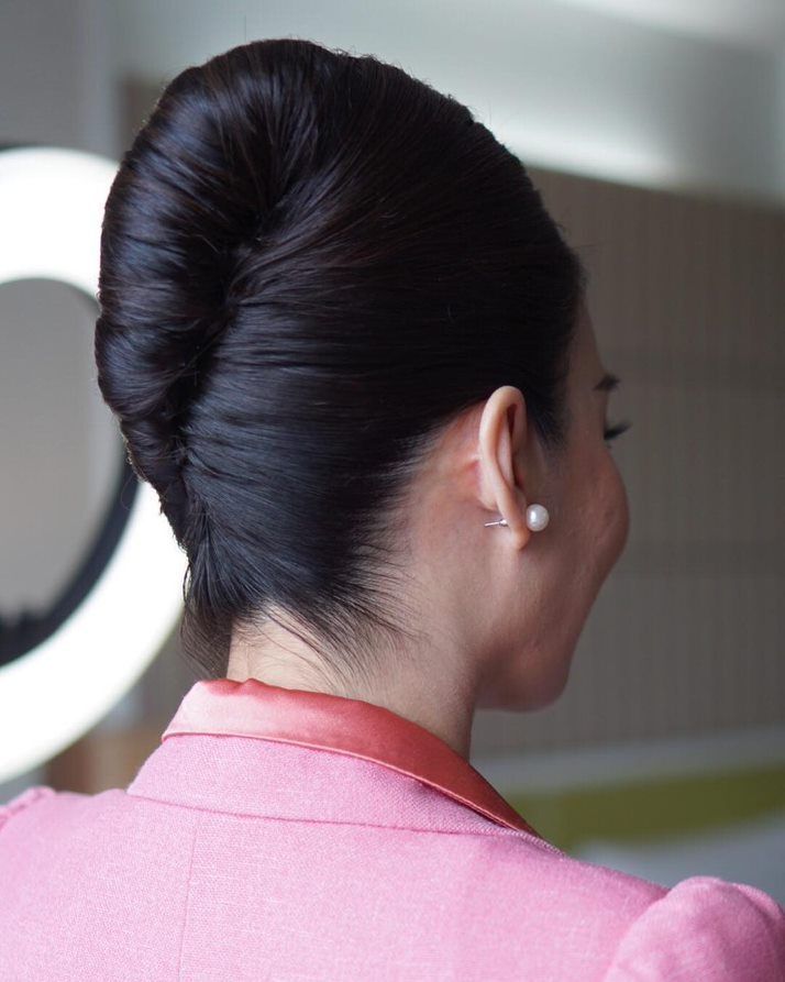A female flight attendant in a pink suit and a French twist.