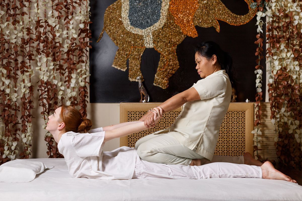A therapist doing Thai massage technique by pulling a woman’s arms.