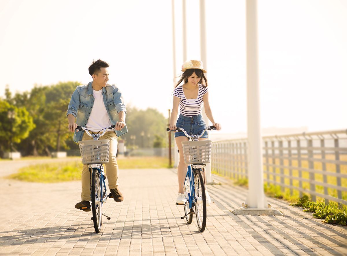 Asian couple riding bicycles together in a park.