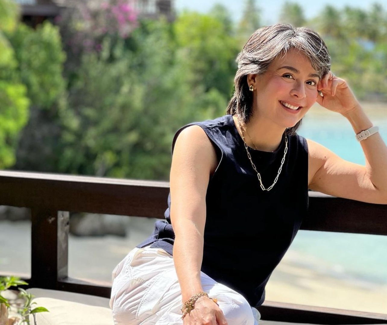 Asian woman with salt and pepper hair wearing a black top and white pants.