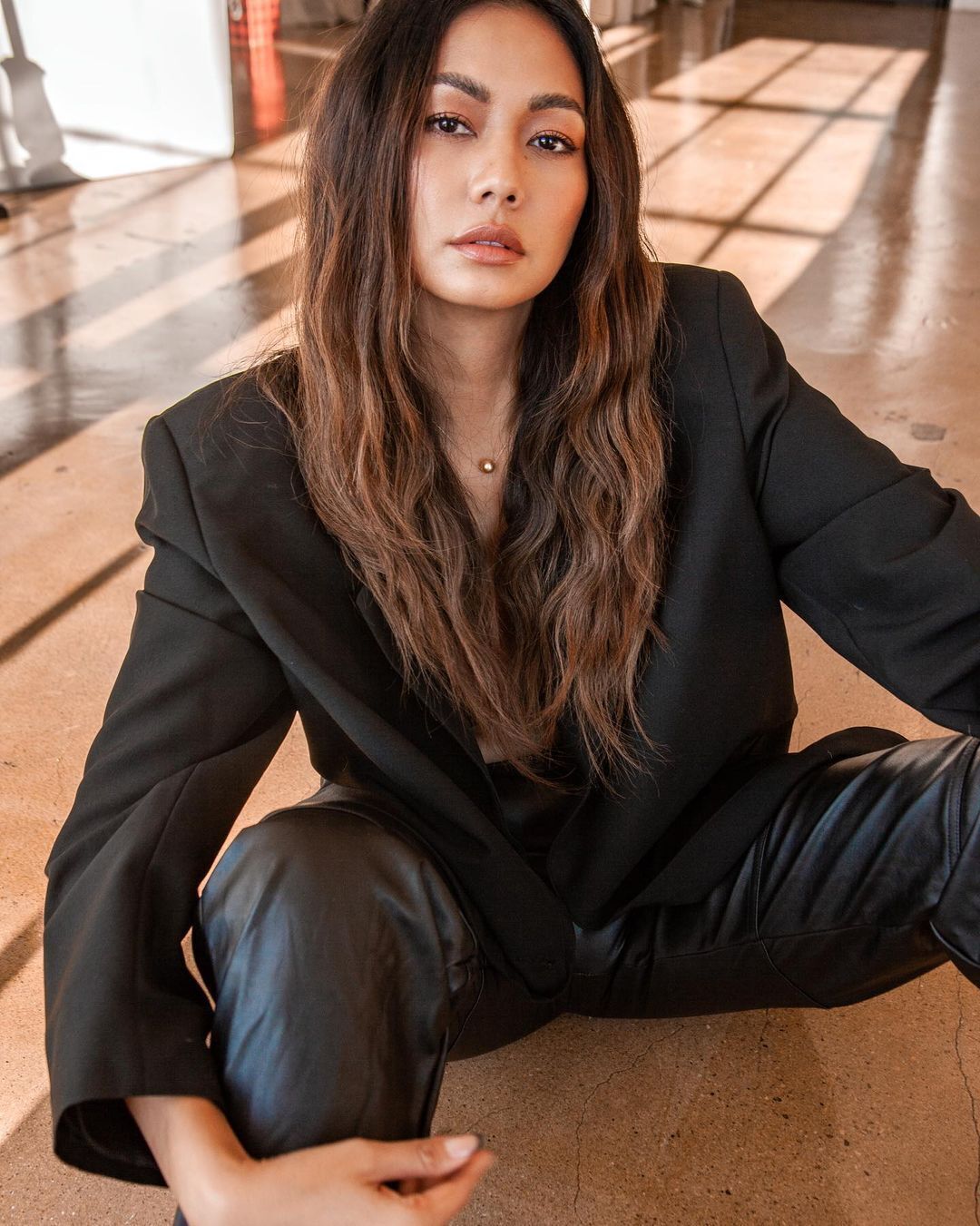 Mica Javier with golden bronze hair highlights and black blazer sitting on the floor.