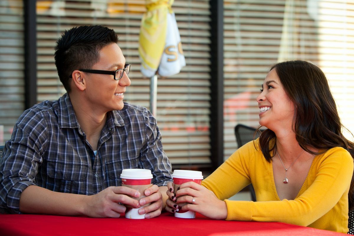 Asian couple smiling at each other while on a coffee date.