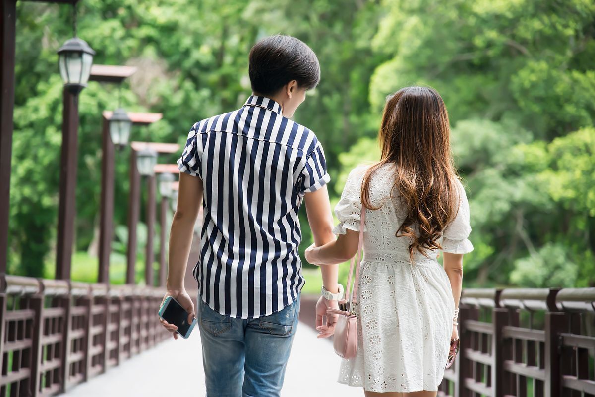 Asian couple walking at a park, with the woman holding on to the man’s arm.
