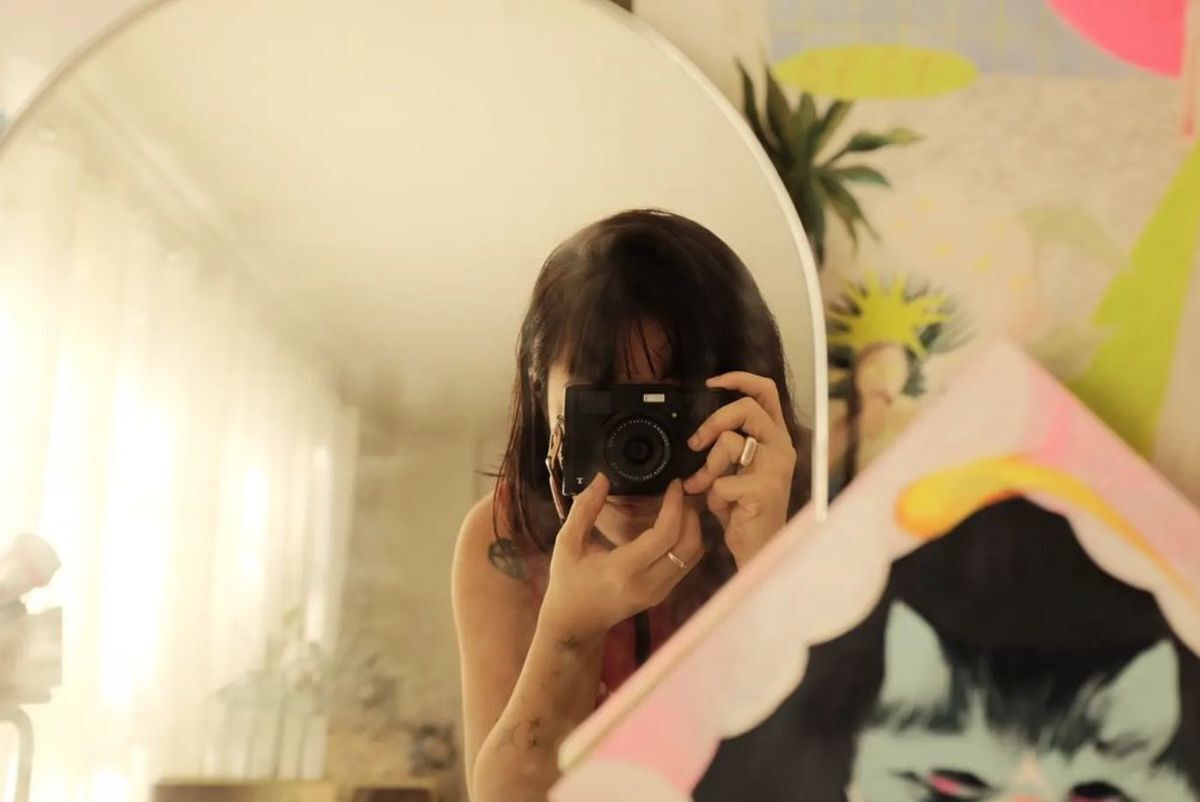 Asian woman taking a self portrait in front of a mirror using a digital camera. 