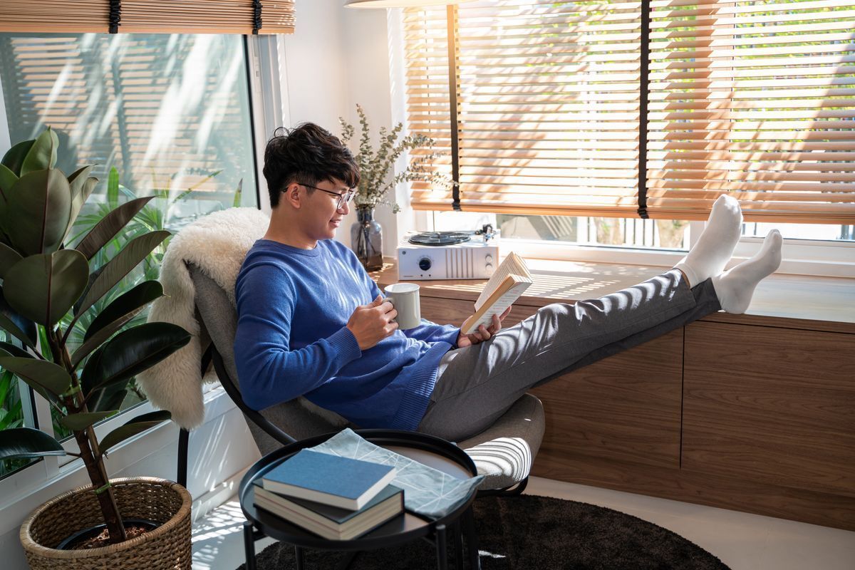 A man relaxing in a chair while reading a book and drinking coffee.