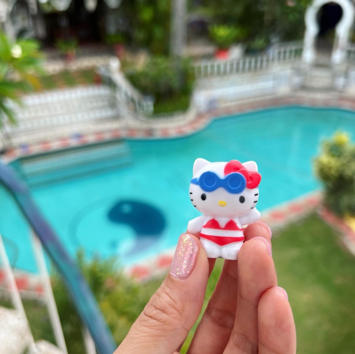 Close up of a hand holding a Hello Kitty toy with swimming pool in the background.