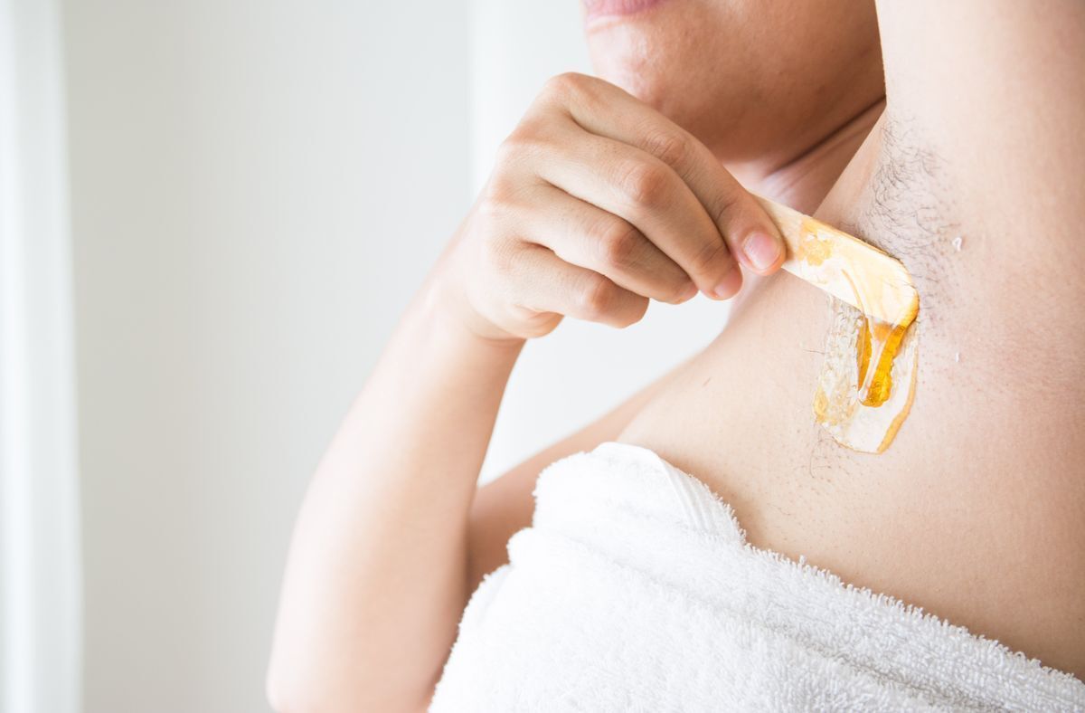 Woman applying melted wax on her armpit with a wooden stick.