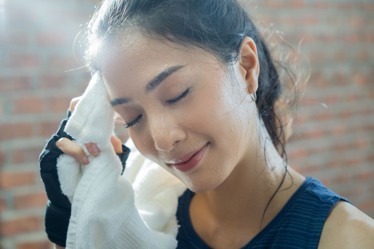 An Asian woman wiping sweat off her face with a clean towel after a workout session.