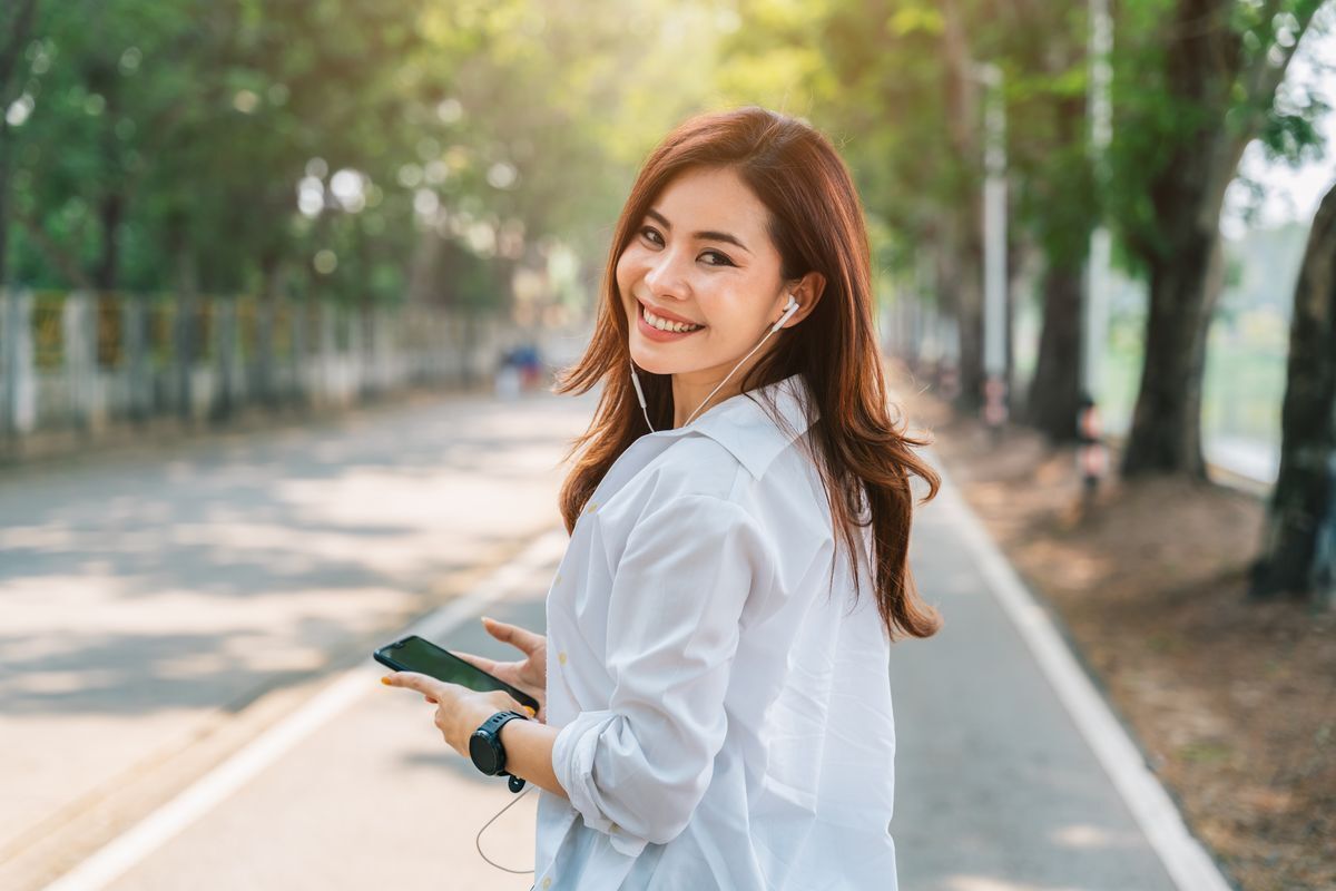 An Asian woman listening to music with wired earphones while taking a walk