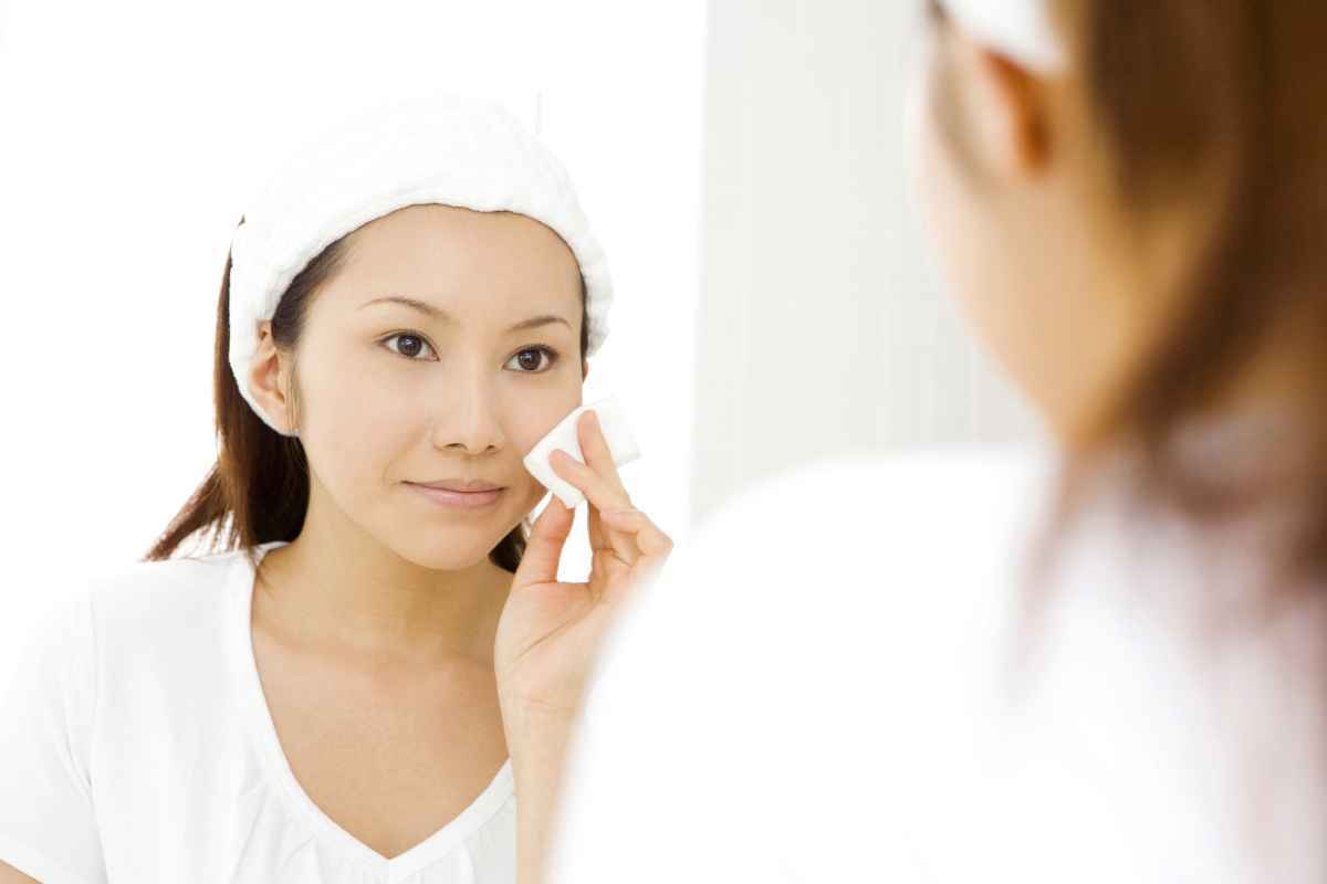 Asian woman wiping her face with a cotton pad.