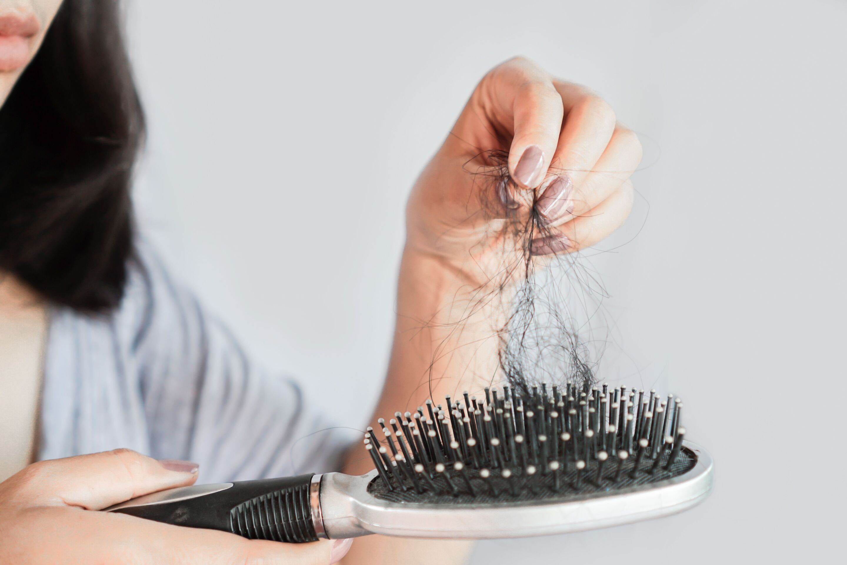 An Asian woman holding a brush with fallen hair