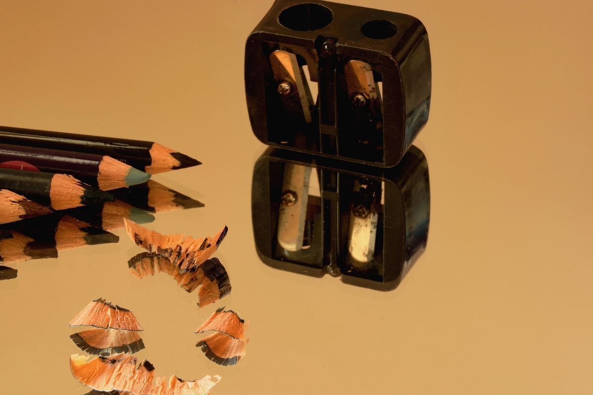 Eye pencils and a black sharpener with their reflections on a mirror.