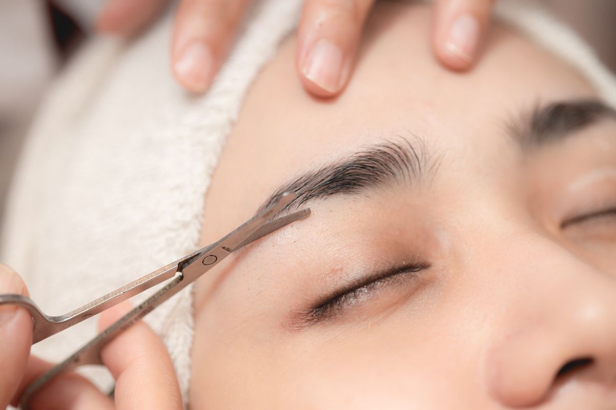 A woman getting her eyebrows trimmed with a pair of small scissors. 