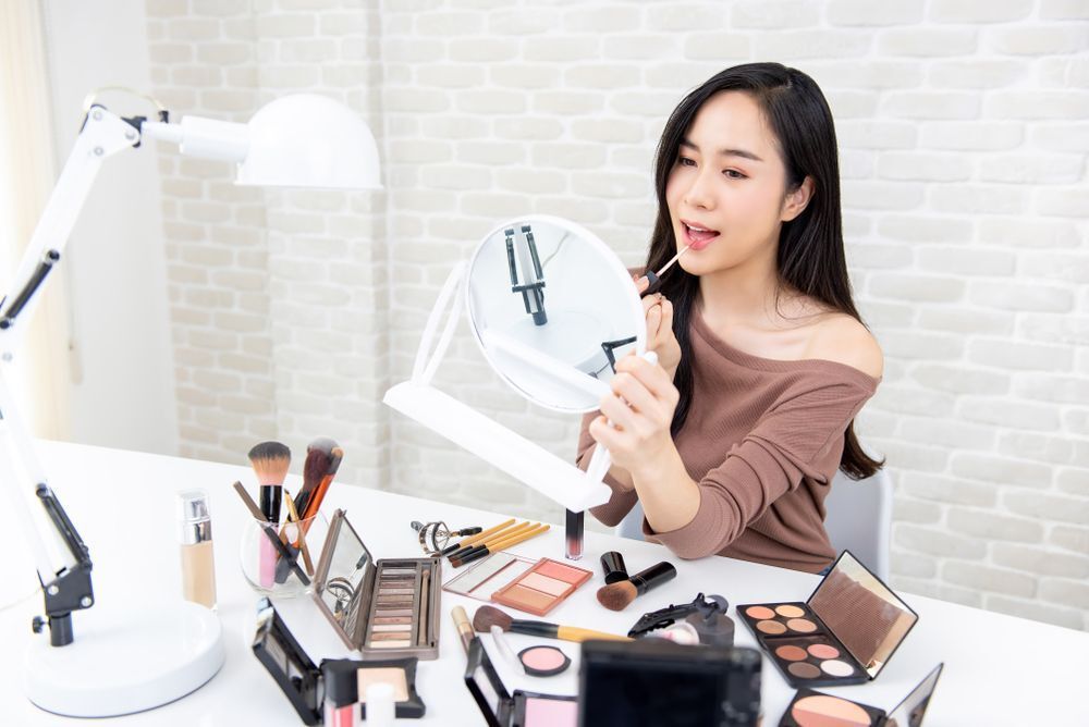 Young Asian woman applying lipstick looking at the mirror.