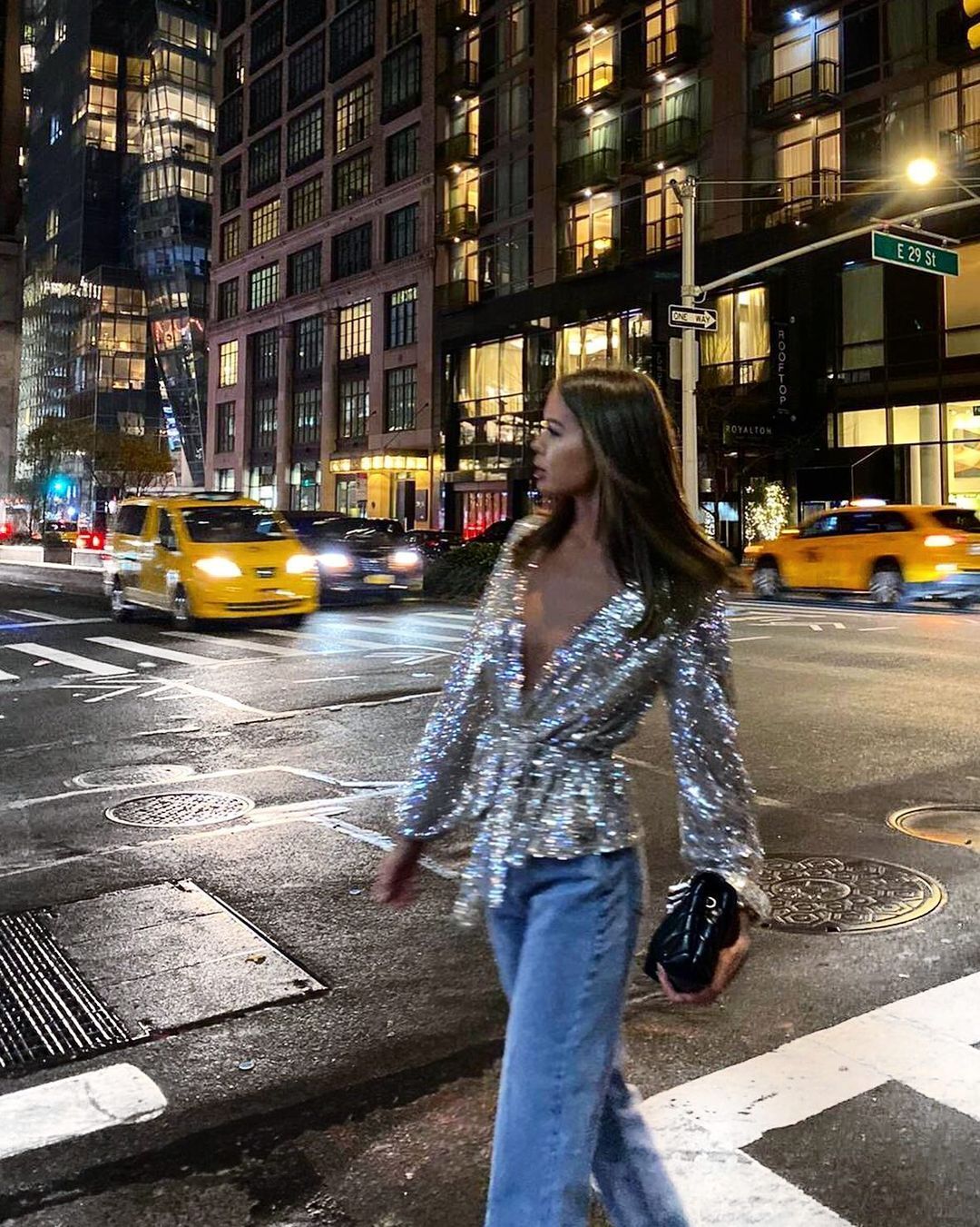 A woman in sequin blouse and jeans walking across the street.