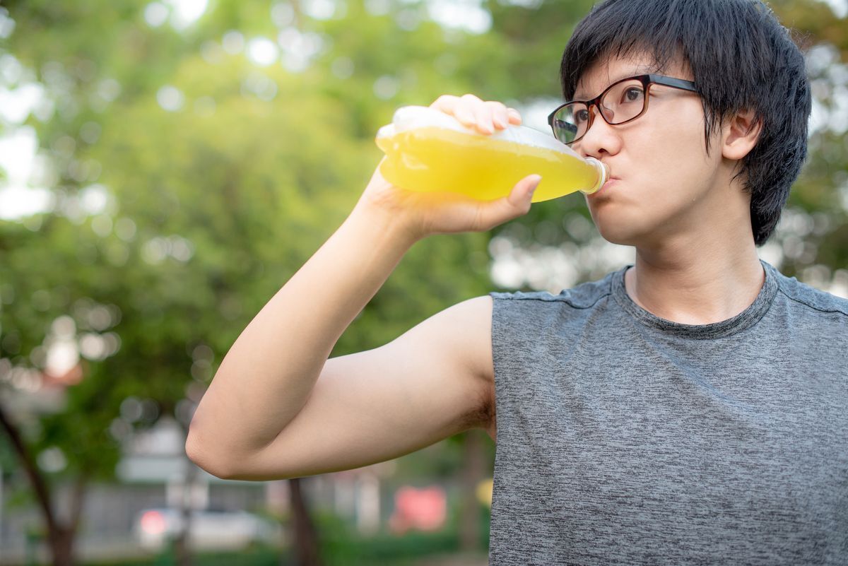 Asian man with eyeglasses is drinking a yellow colored drink.