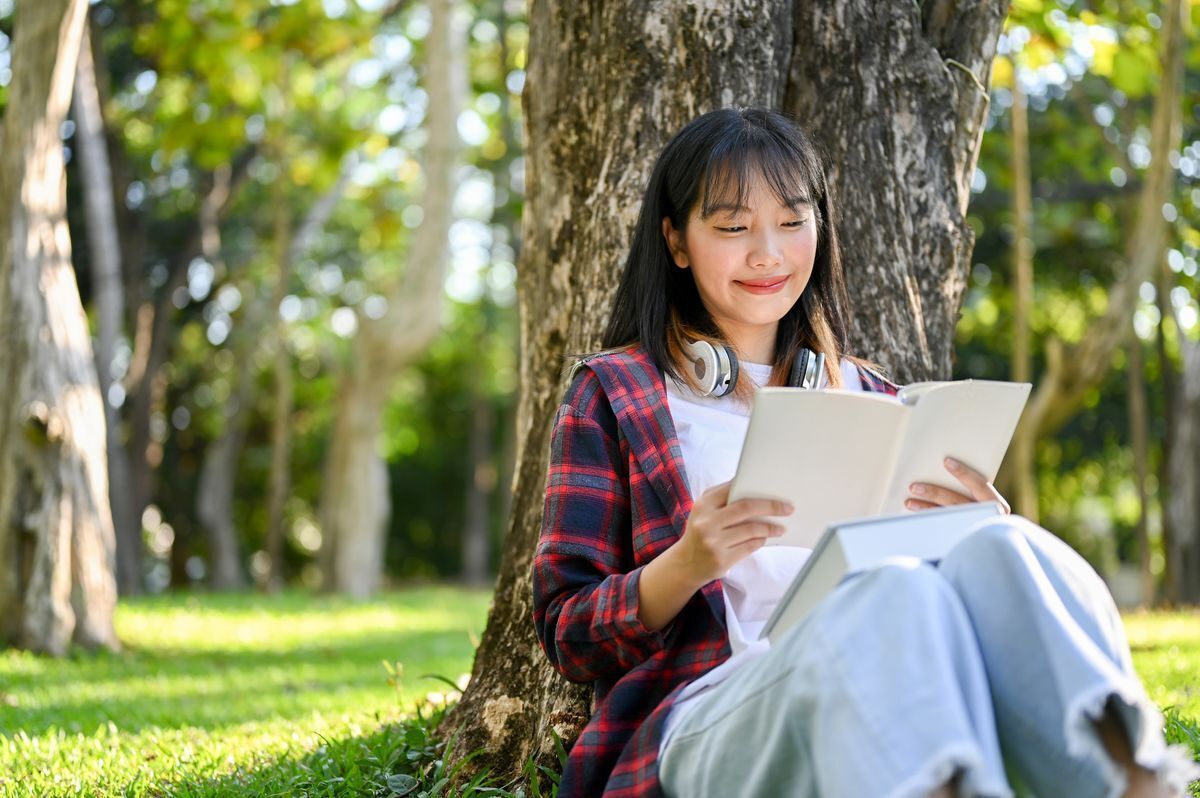 Asian girl reading a book on grass. 