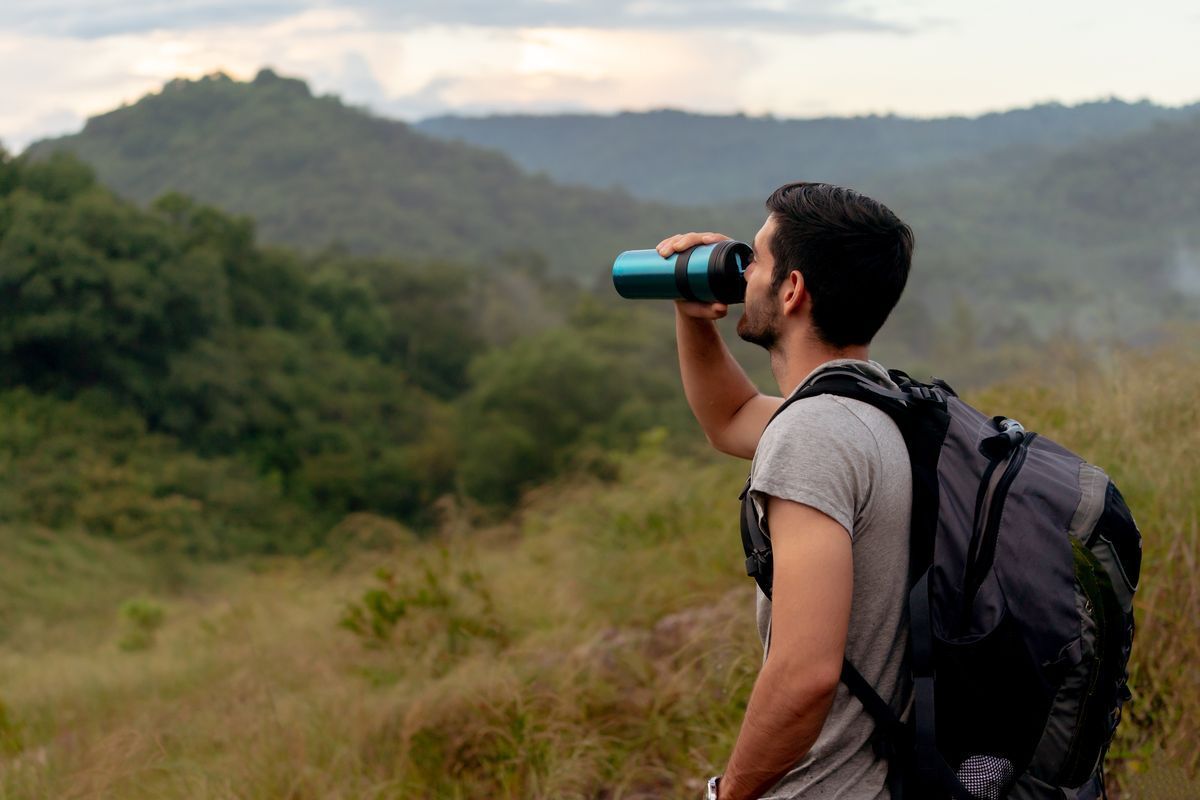 A man drinks from a refillable water bottle while on a hike