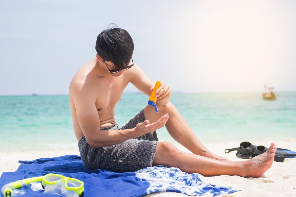 A man applies sunscreen while sitting on a towel at the beach