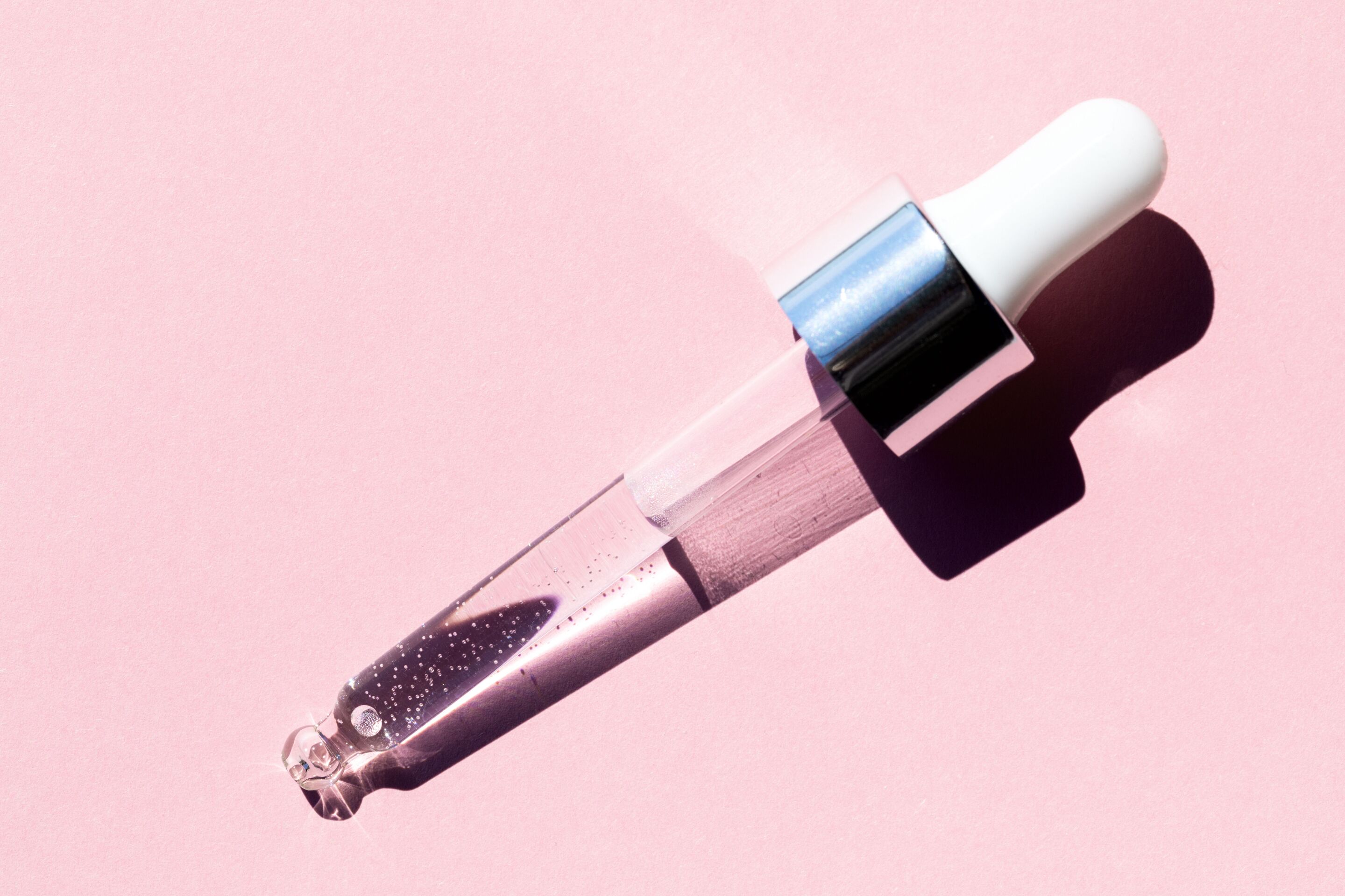 Dropper with serum inside against pink backdrop 