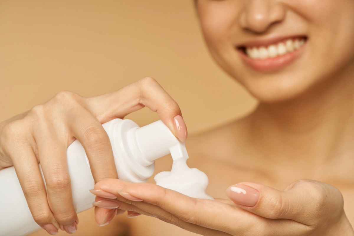 A smiling woman dispensing a foamy cleanser into her hand.