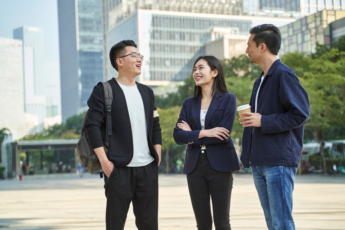 An Asian woman with two male colleagues chatting outside.