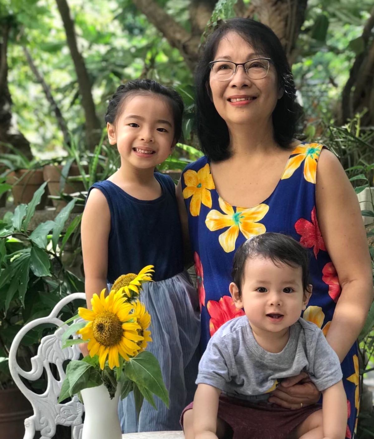 Asian woman smiling with a young boy and a girl against a background of greenery. 