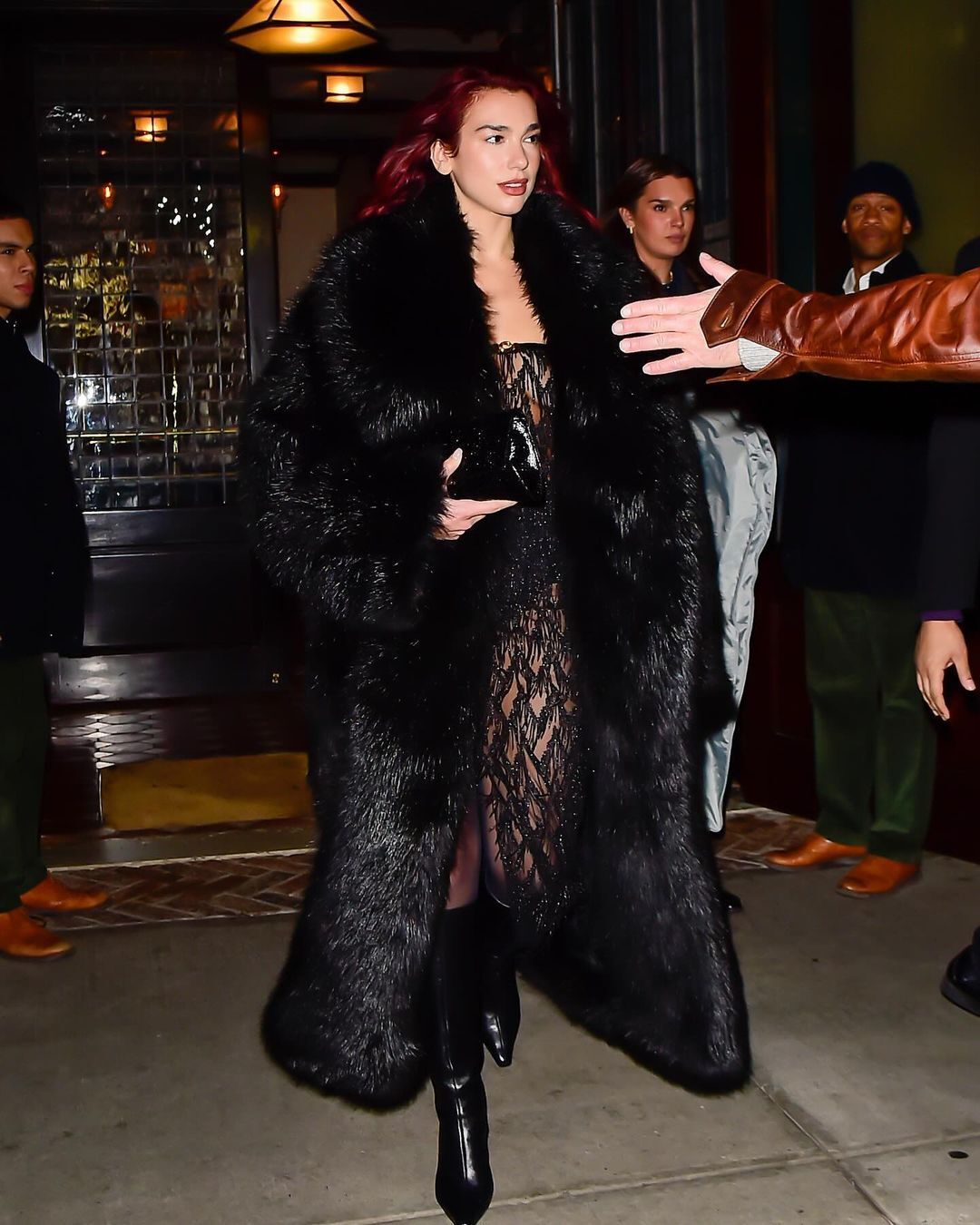 Dua Lipa wearing lacey dress, fur coat, and boots.