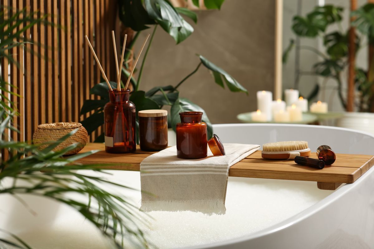 A wooden bath tray with wellness items over a bubble bath. 