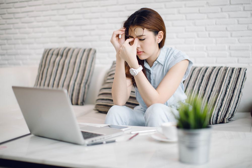 An Asian woman sitting in front of a laptop and massaging her nose bridge