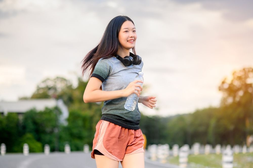 Smiling woman holding a water bottle while jogging at the park.