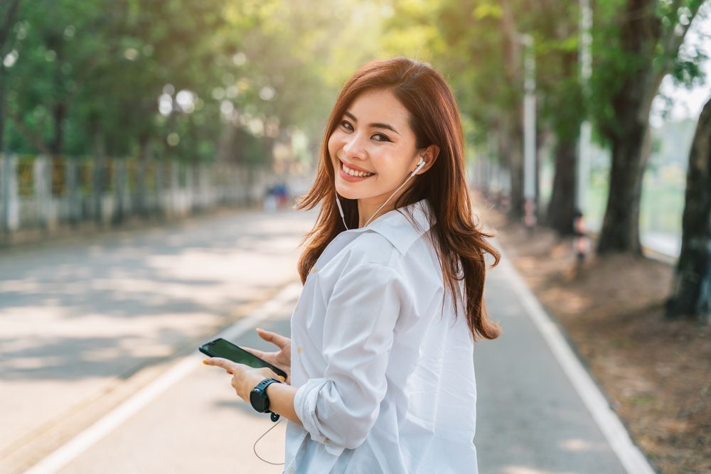 Smiling woman listening to music from her phone while walking outdoors.