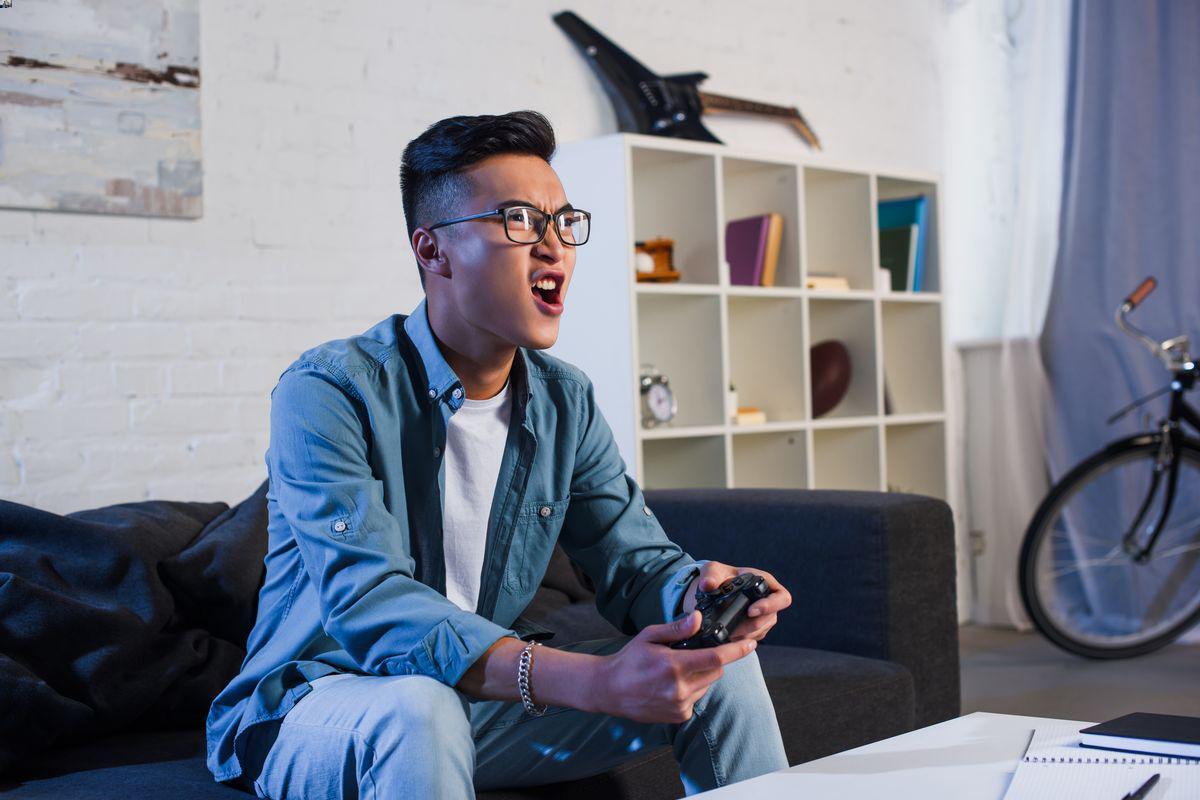 Asian man playing video games in bachelor pad 