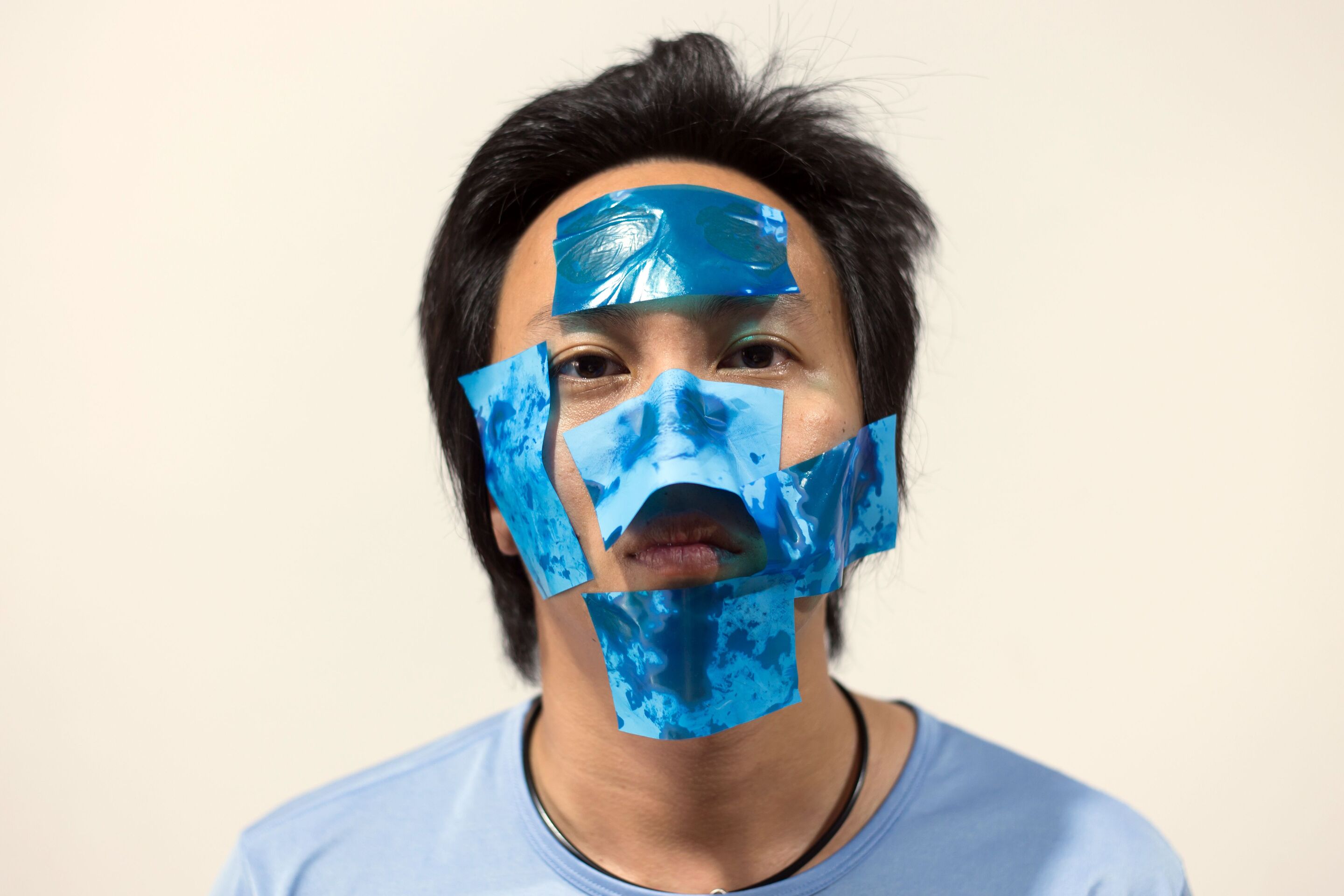 An Asian man with blue oil blotters on his face