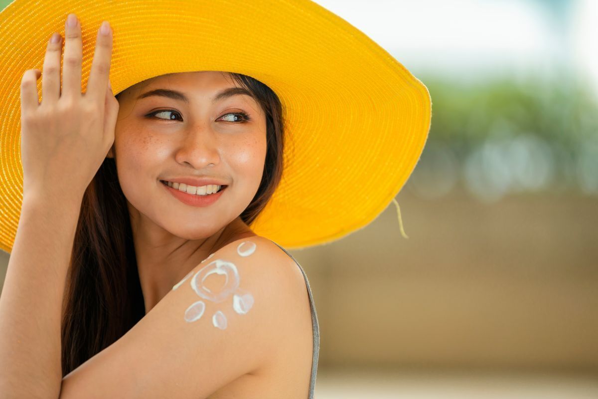 An Asian woman smiling with a drawing of the sun on her forearm outlined in sunscreen.