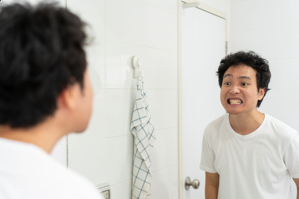  Asian man looking at teeth in mirror
