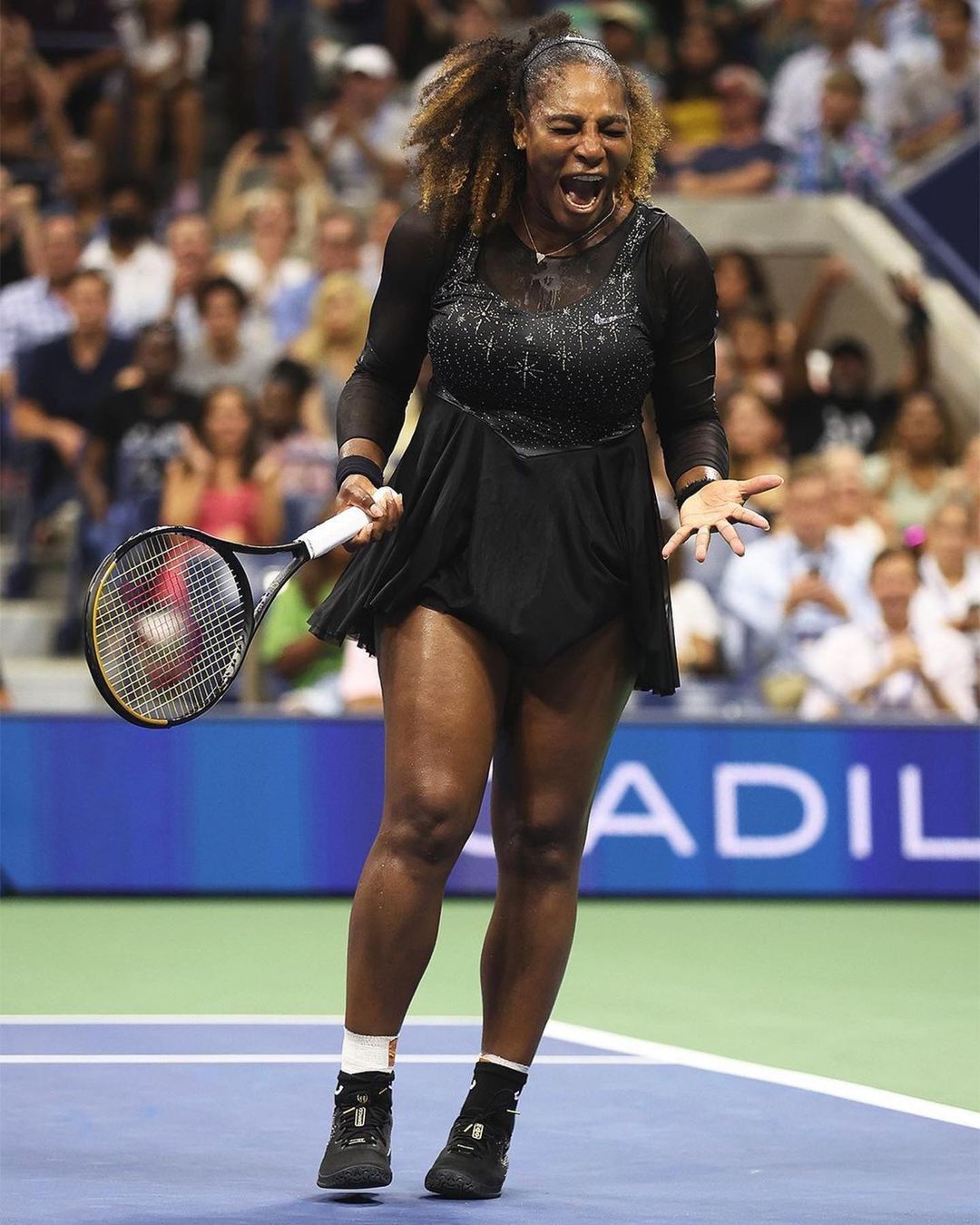 A portrait of Serena Williams in a black tennis clothing set at a tennis tournament.
