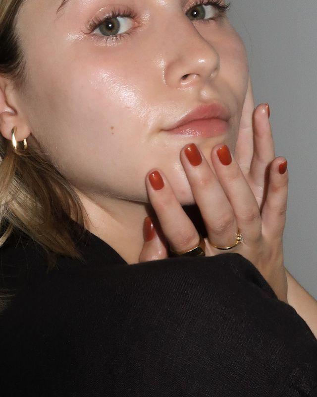 Close up pose of a woman in a black top and her red polished fingernails touch her face 