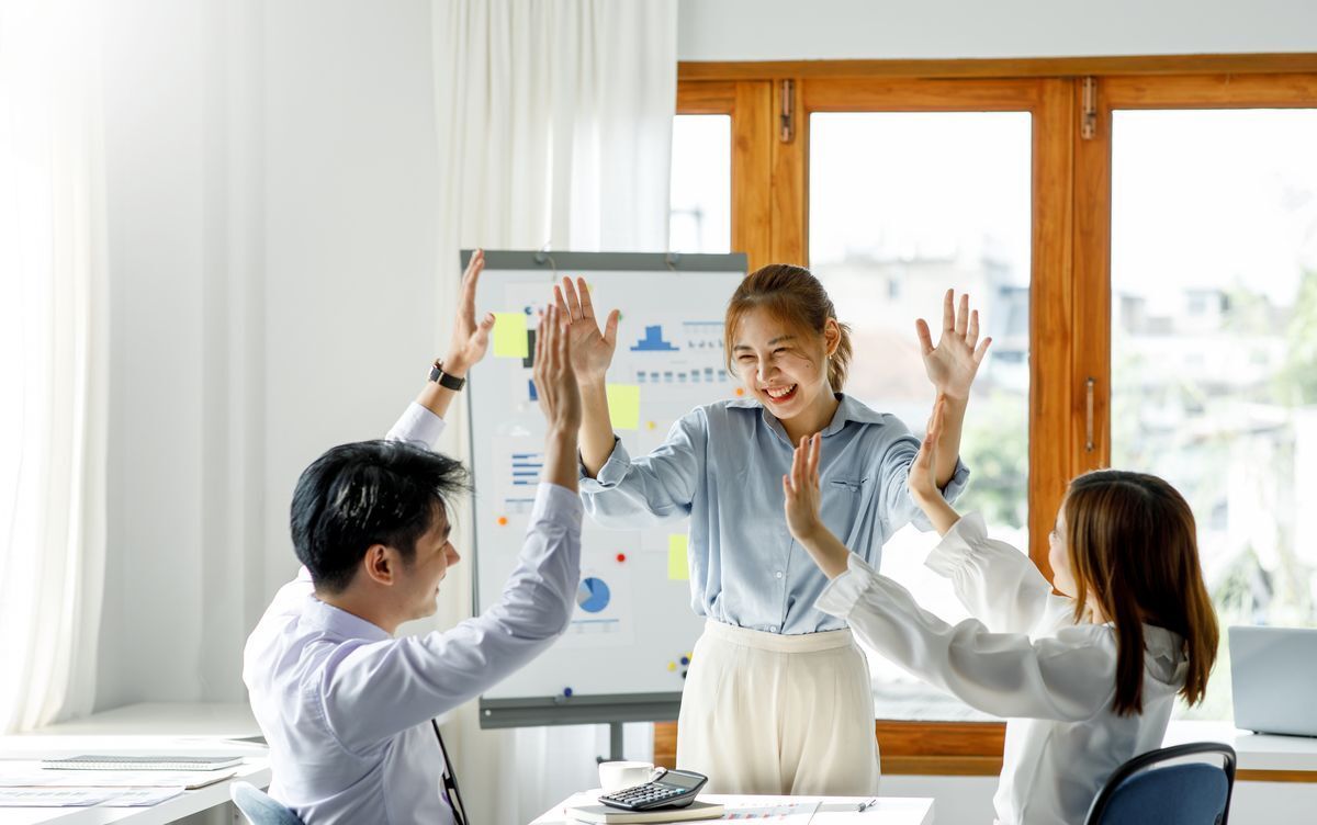 Asian woman high-fiving peers at work.
