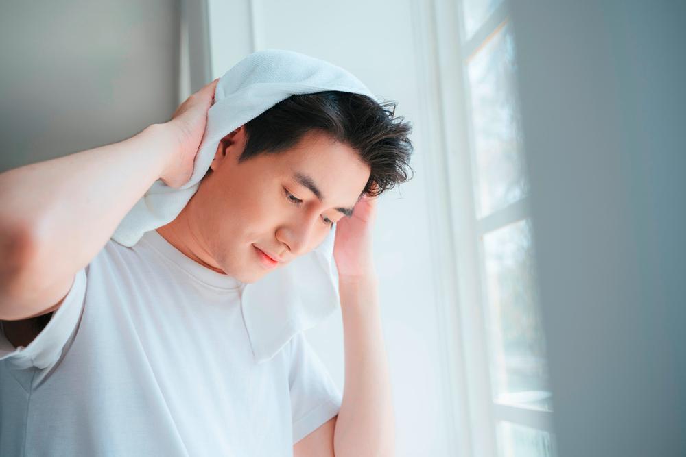 Asian male professional raises one arm in triumph as he holds a laptop in his other arm.
