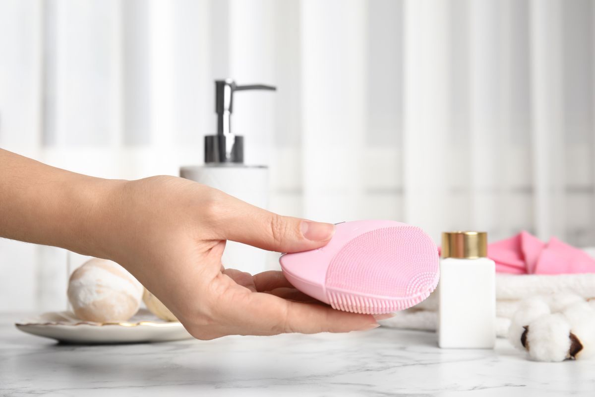 A woman holding a facial cleansing brush over a marble table. 