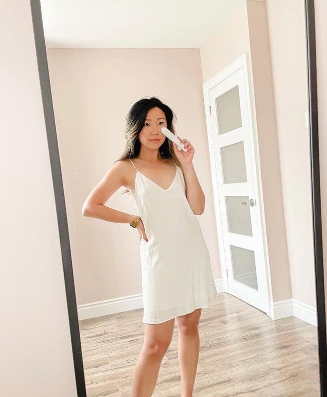 A woman using a handheld eye massager in front of a mirror.