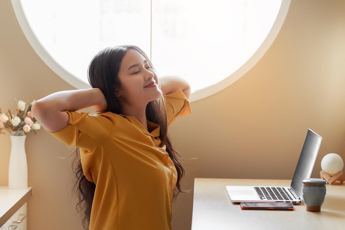 Asian woman stretching to relax in front of laptop